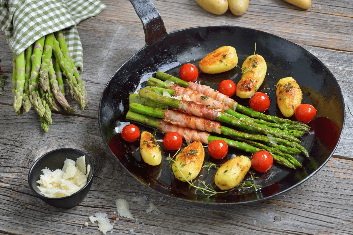 A skillet filled with asparagus, tomatoes, and potatoes on a wooden table