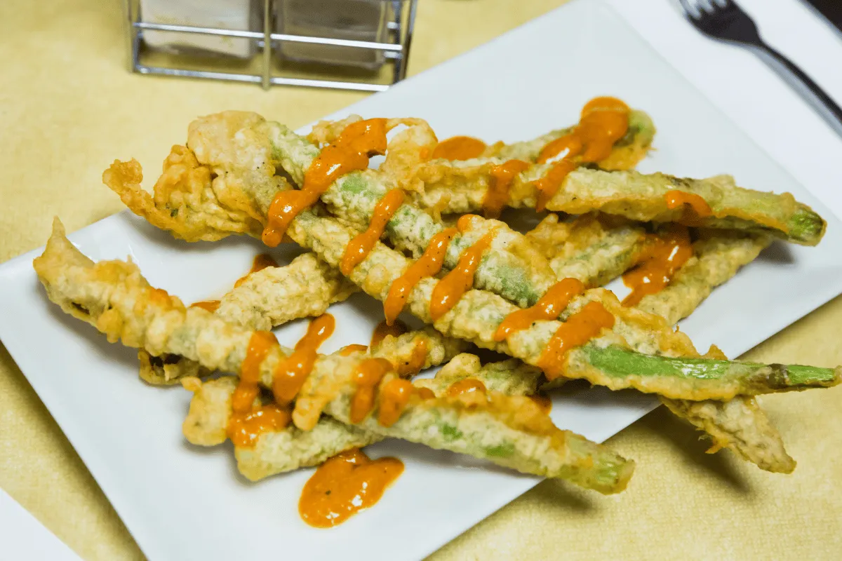A white plate with a serving of fried asparagus spears. The asparagus is green and crispy, with a light tempura batter coating