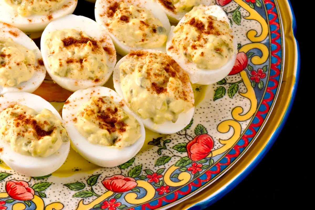 Close-up photo of a plate filled with deviled eggs. The eggs are light yellow and decorated with a piped pattern.