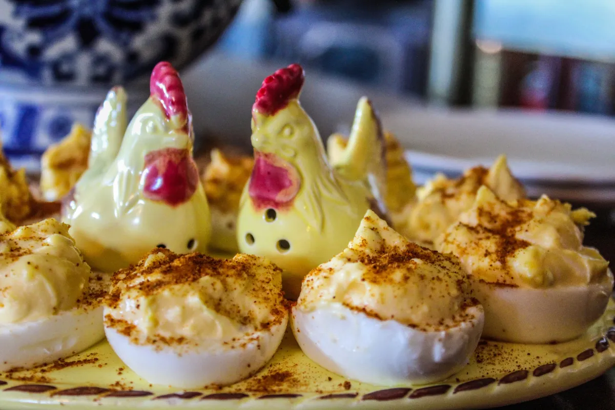  A plate of devilled eggs with a yellow filling, garnished with paprika. There are two chicken-shaped salt and pepper shakers on the plate.