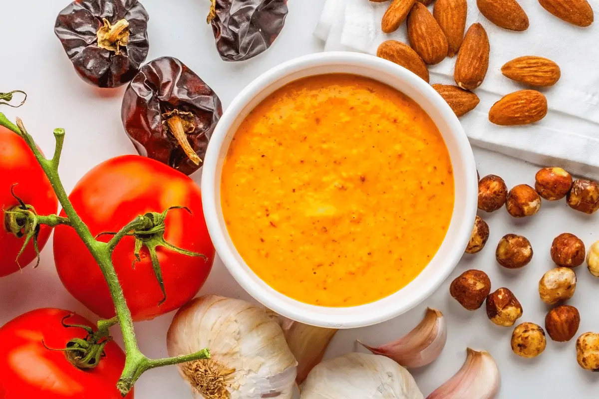 Glass bowl of creamy Boom Boom Sauce surrounded by ingredients with dishes like fries, burgers, and shrimp in the background, highlighting its versatility and flavor